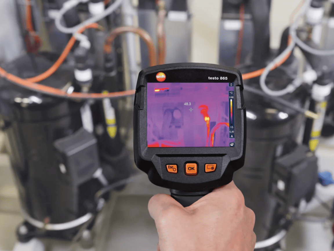 testo 865s Thermal imaging device being held in a hand with a blurred industrial background