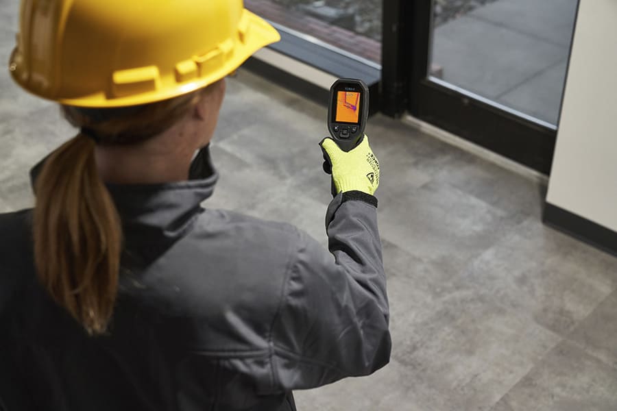 Person wearing a yellow hard hat and gloves using a TG165-X thermal imaging device.