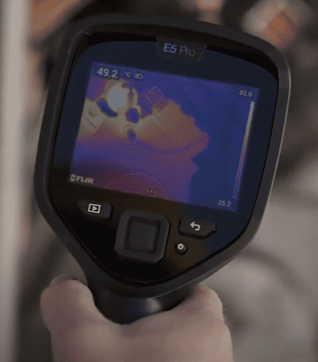 Flir e6 Thermal imaging device with a screen displaying thermal images, held by a person.
