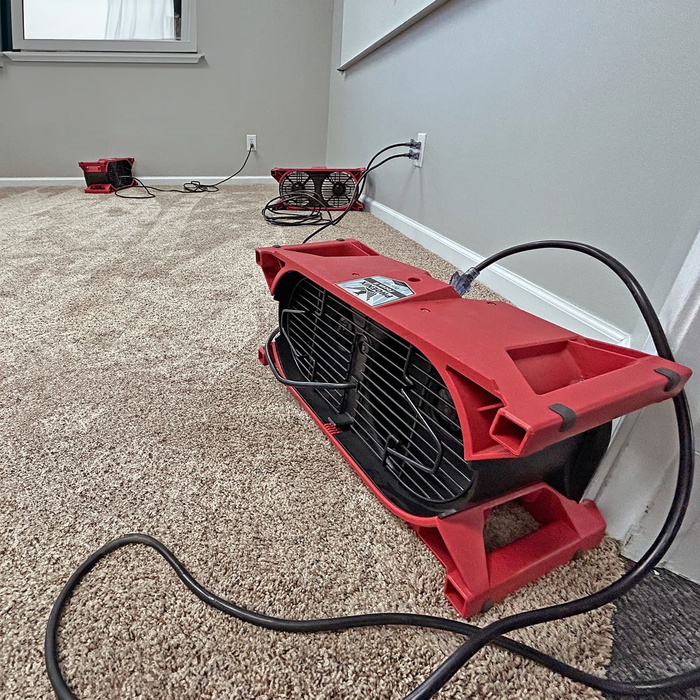 Red Phoenix Focus II Dual Axial Air Movers on a carpeted floor with visible power outlets.