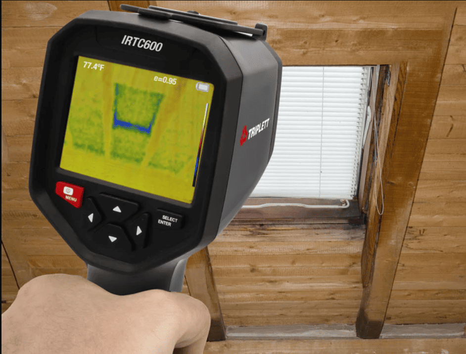 IRTC600 Thermographic camera held by a person in front of a window with wooden framing.