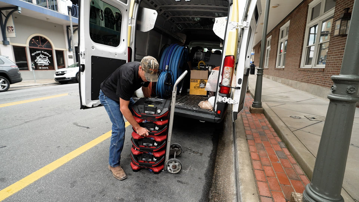 Man loading a stack of BLE AirMax Phoenix Radial Air Movers onto the back of a van on a city street.