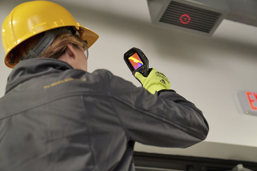 Person wearing a hard hat and safety glasses using a TG165-X thermal imaging device.