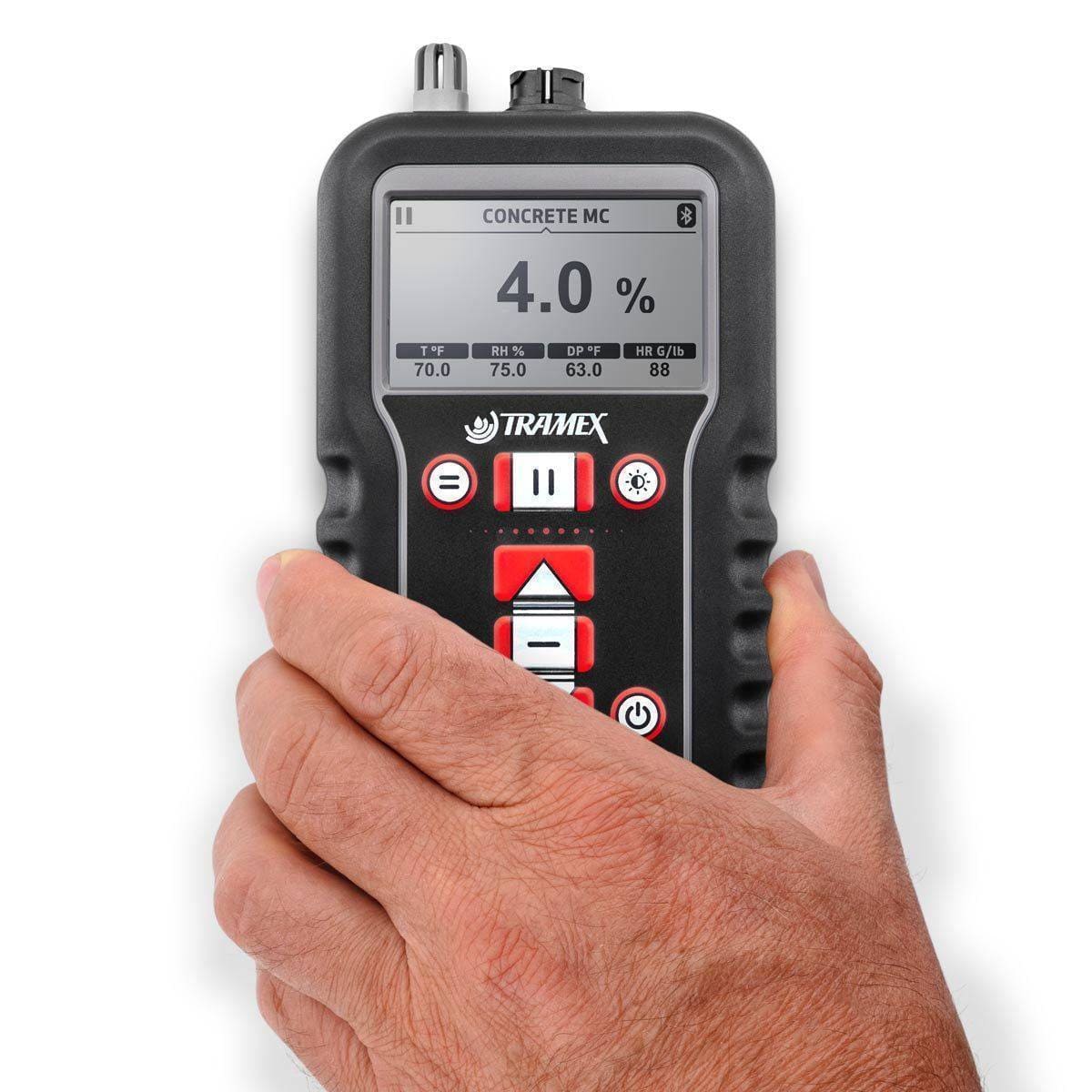 Hand holding a digital tramex concrete x5 concrete moisture content measurement on a white background