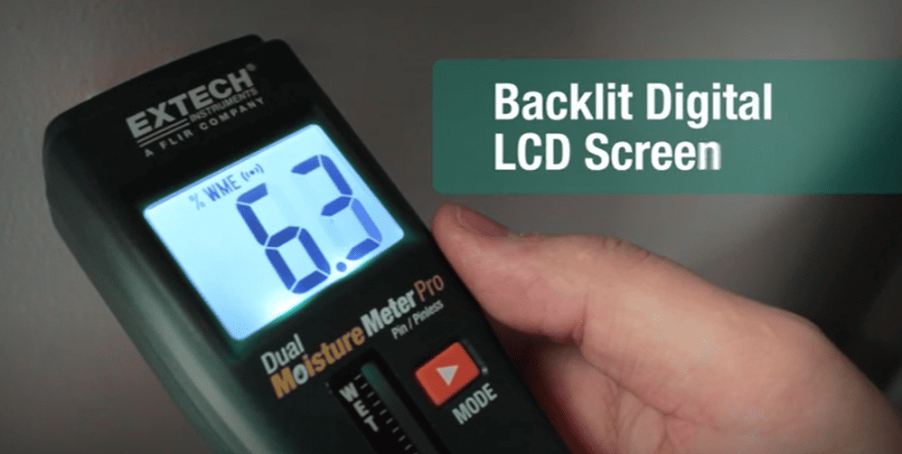 Extech mo260 digital moisture meter with backlit LCD screen being held by a hand.
