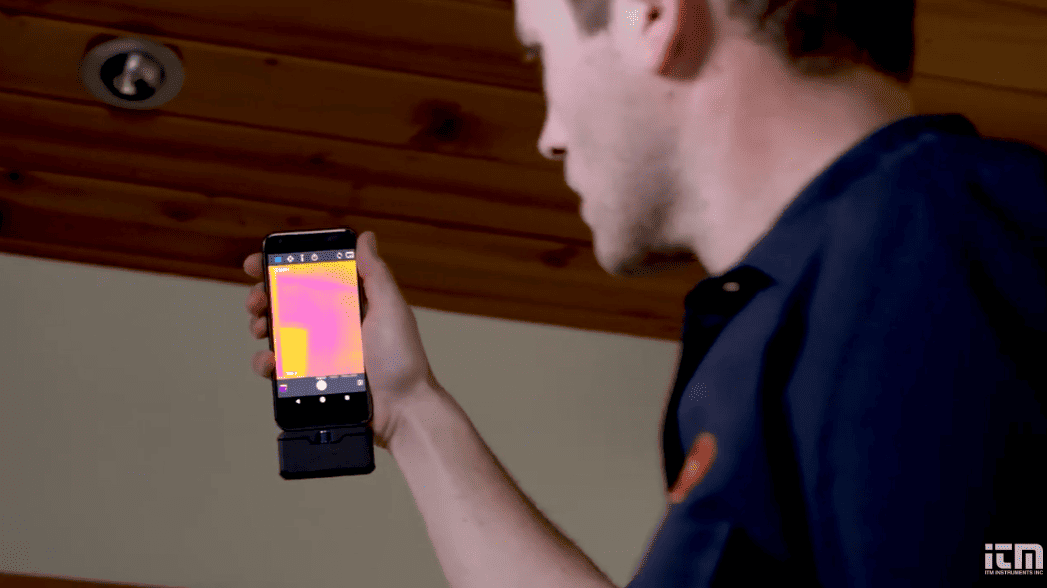Person holding a smartphone displaying a thermal imaging app in an indoor setting using flir one pro micro usb
