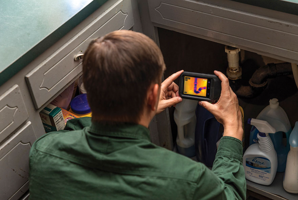 Person using a smartphone with flir c3 x thermal imaging app to inspect kitchen cabinets.