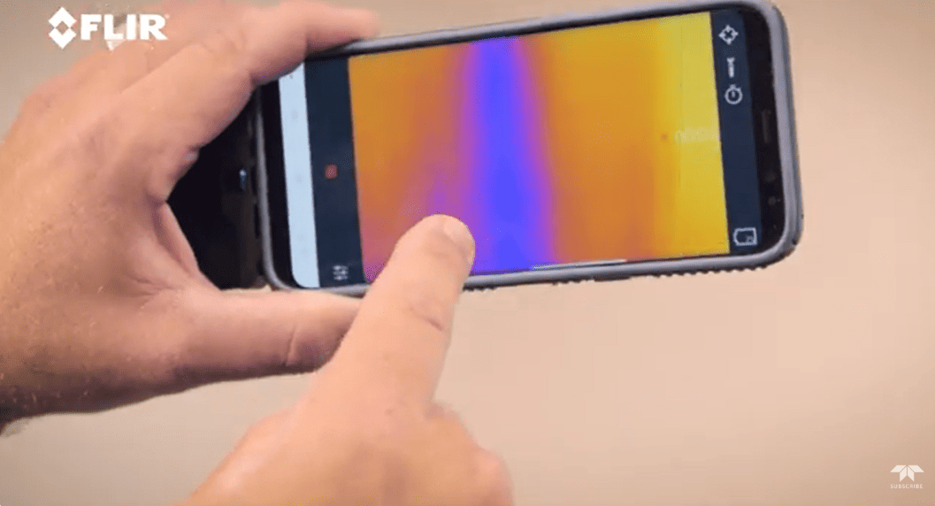 Hand holding a smartphone with FLIR ios pro thermal imaging app on a plain background