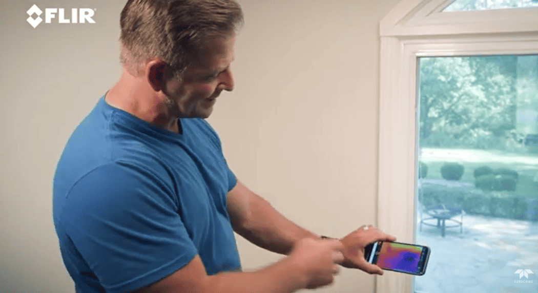 Man using a smartphone with FLIR one pro app to check temperature on a window
