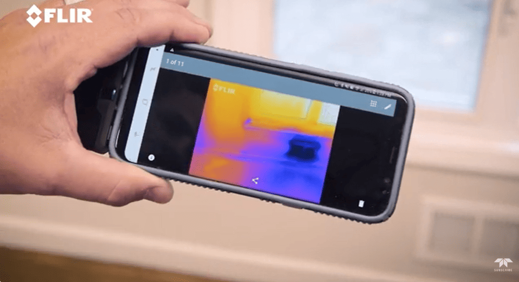 Hand holding a smartphone with flir one pro thermal imaging app displaying temperature readings on a surface.