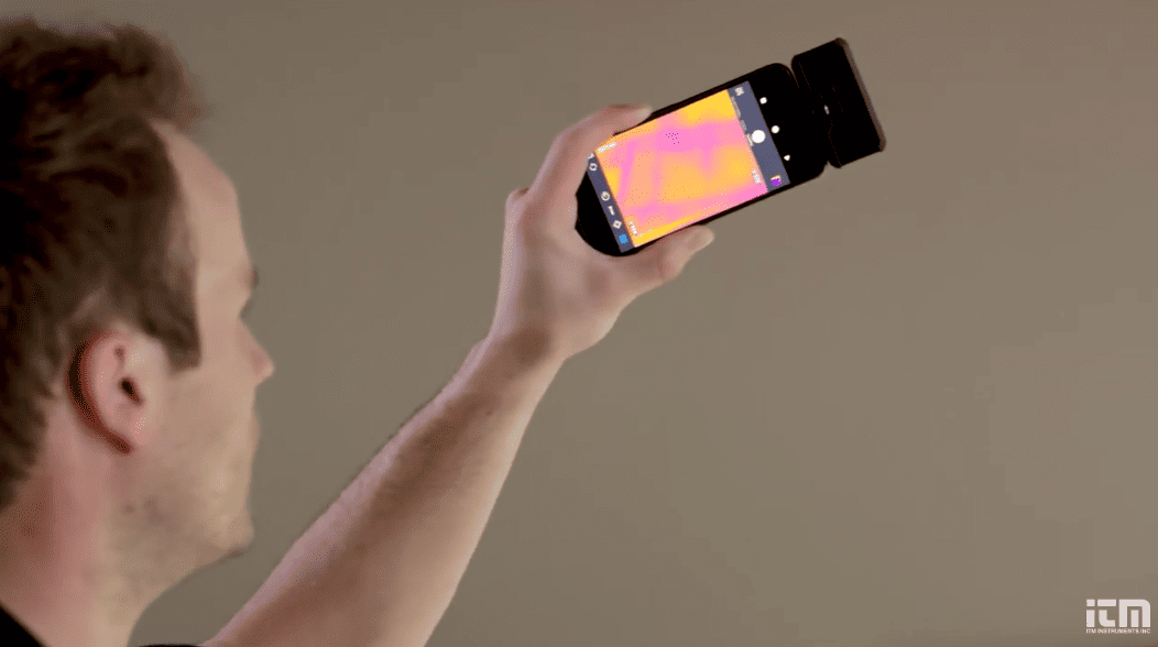 Person holding a smartphone with flir one pro micro app display against a plain background
