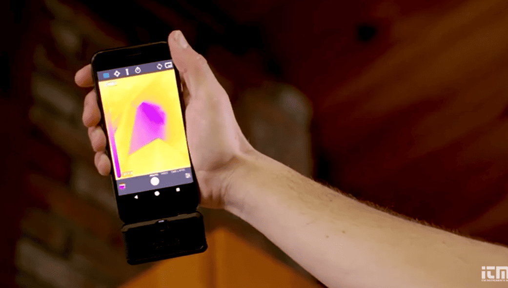 Hand holding a smartphone with a flir one pro micro usb thermal imaging app on the screen, displaying a purple image.