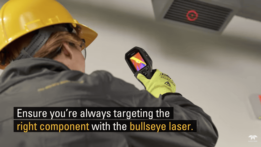 Person wearing a hard hat and safety glasses using a flir tg165 x thermal camera with a bullseye laser on a ceiling.