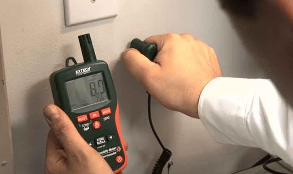 Person using a digital mo290 extech to measure moisture on a wall.