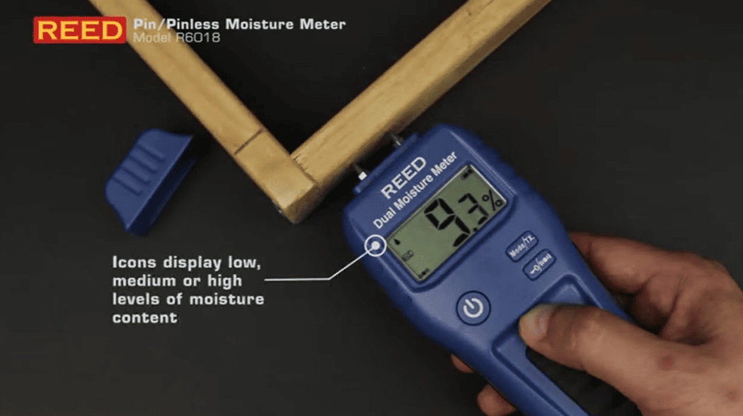 REED r6018 dual moisture meter being used on a wooden board with digital display showing moisture content.