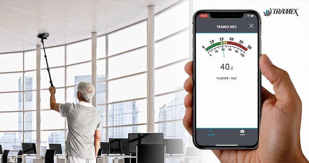 Person using a smartphone app for humidity measurement in an office setting with Tramex ME5 branding.