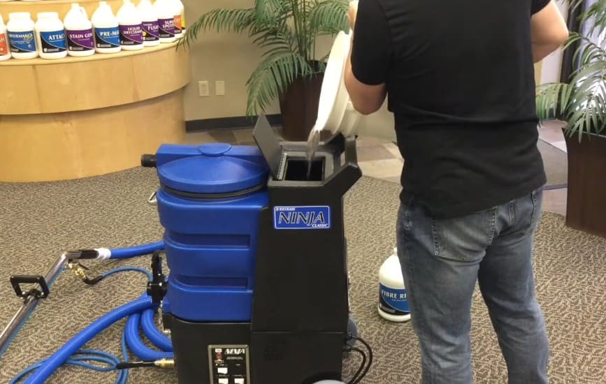 Person using a blue and black vacuum cleaner labeled Ninja 150 in an indoor setting.