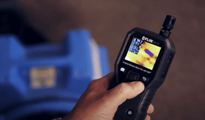 Hand holding a  FLIR_MR176 thermal imaging device with a blurred background