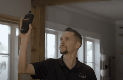 Man holding a MR277 against a wall in a room with large windows.