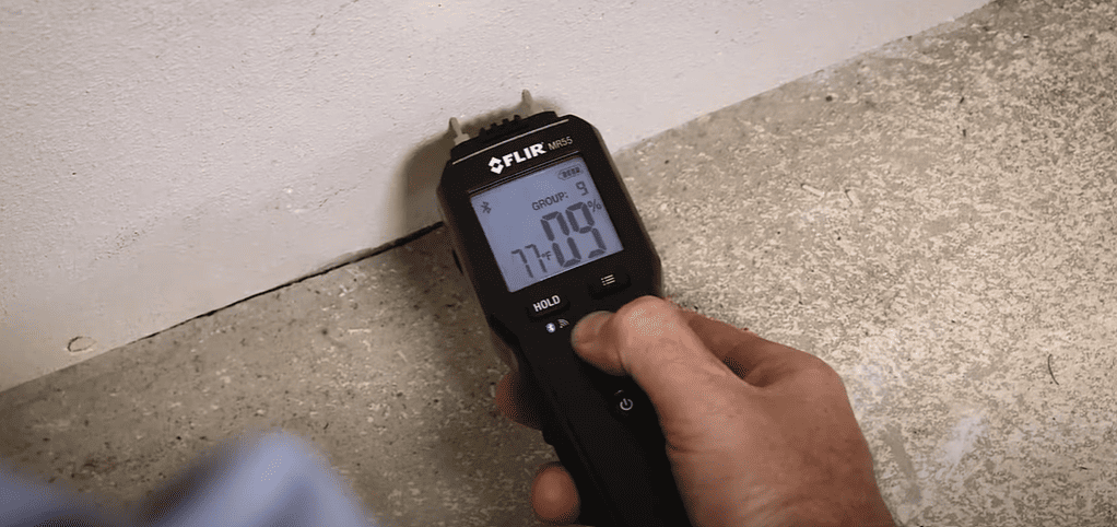 hand holding a mr55 Moisture Meter thermal imaging device against a concrete floor