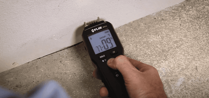 hand holding a mr55 Moisture Meter thermal imaging device against a concrete floor