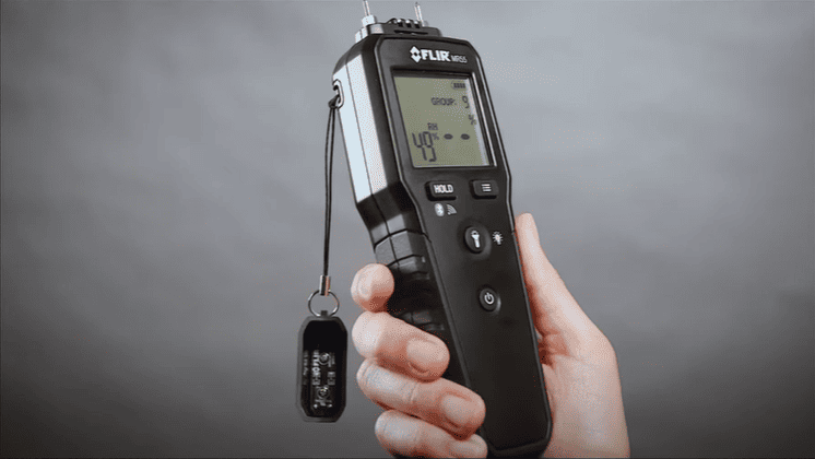 a hand holding Flir mr55 thermal imaging device against a gray background