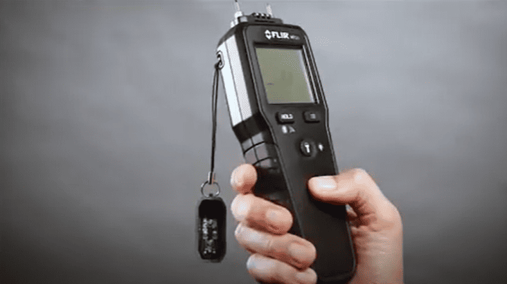 hand holding a Moisture Meter MR55  against a gray background