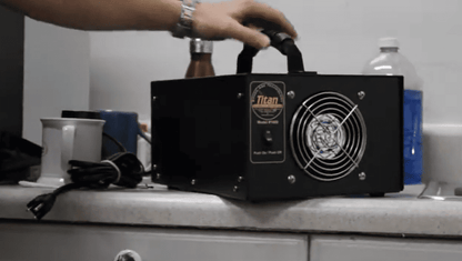 Black Generator Titan 1000 labeled 'Titan' on a kitchen counter with a hand holding it.