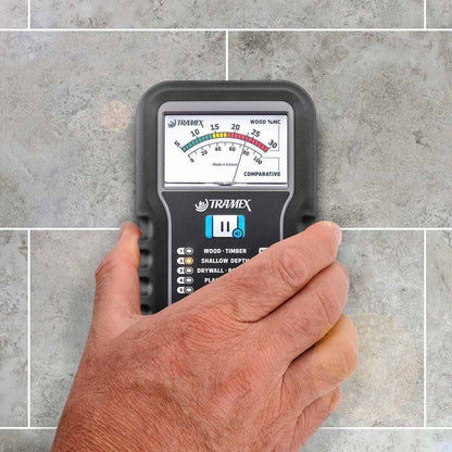 Hand holding a Tramex ME5 moisture meter against a tiled wall background