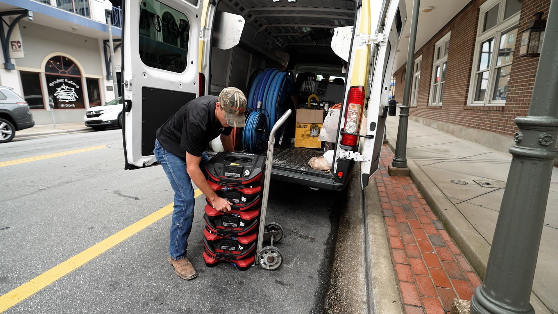 Man loading a stack of BLE AirMax Phoenix Radial Air Movers onto the back of a van on a city street.