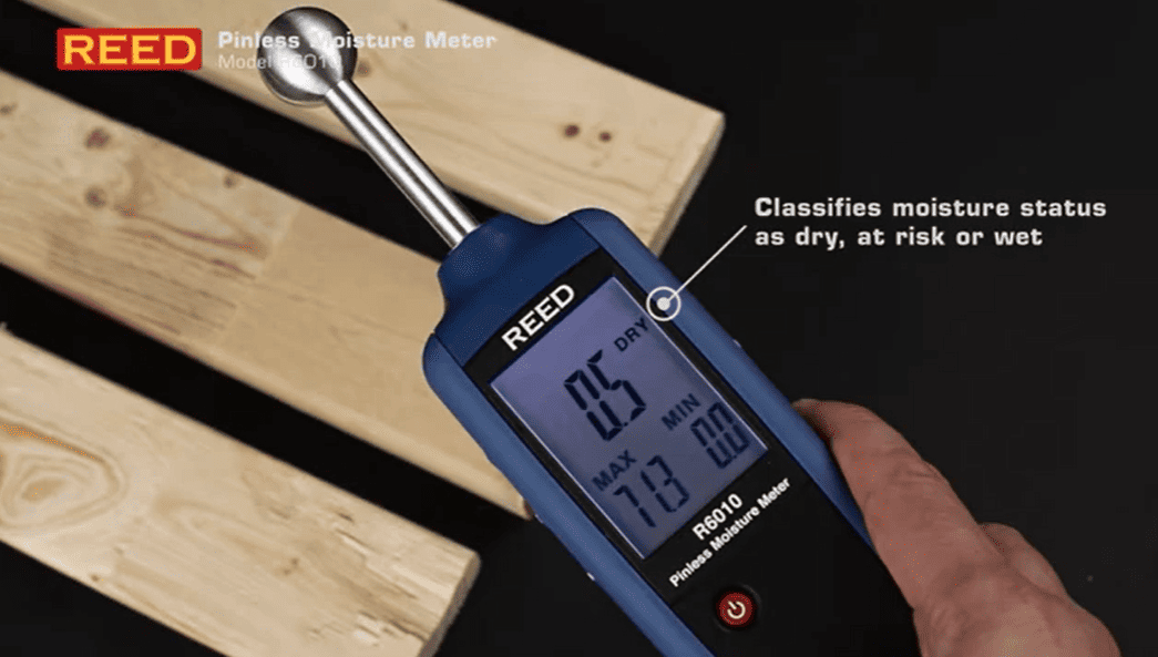 REED R6010 Pinless Moisture Meter being used on wooden planks with digital display.
