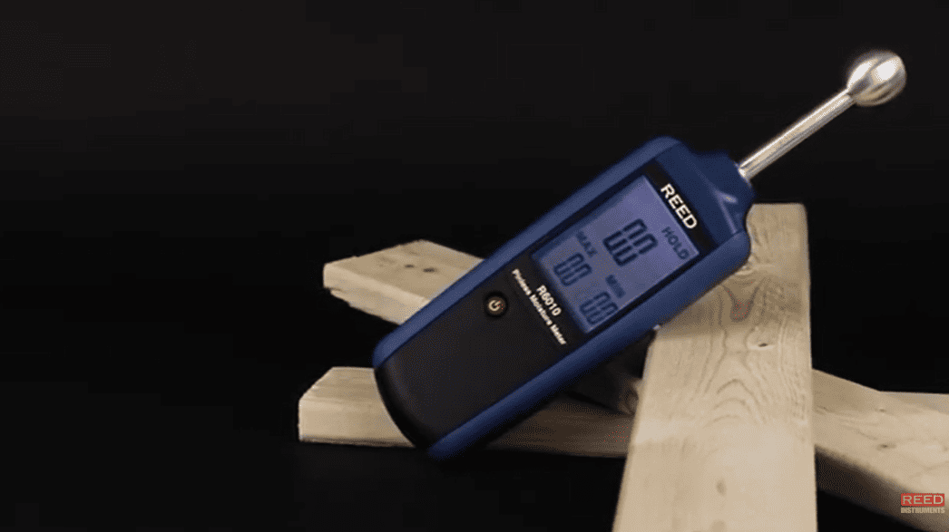 Digital moisture meter on a wooden block with a dark background