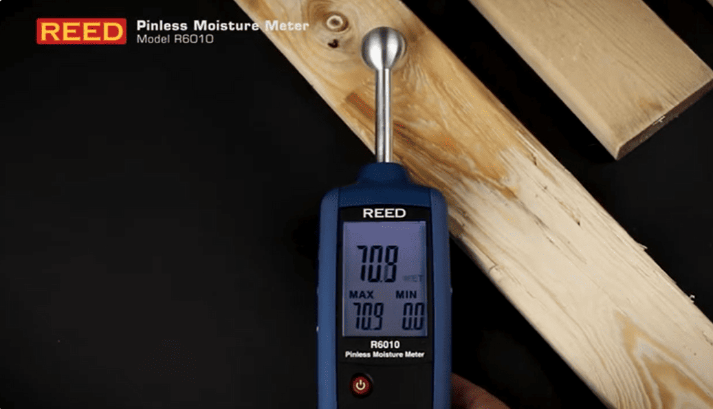 REED R6010 pinless moisture meter on a piece of wood with digital display showing readings.