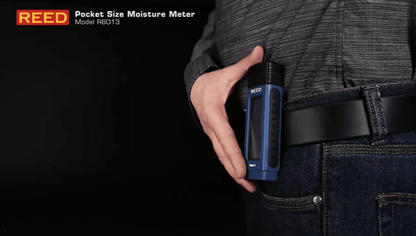 Hand holding a blue REED r6013 pocket-size moisture meter against a dark background