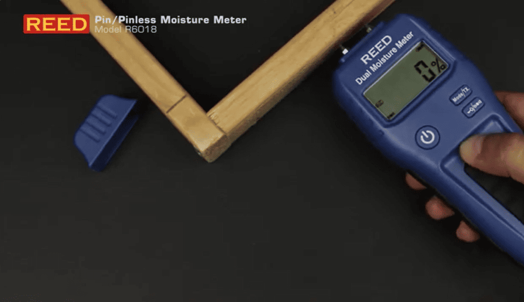 REED R6018-KIT REED Pin/Pinless Moisture Meter being used on a wooden board with a dark background