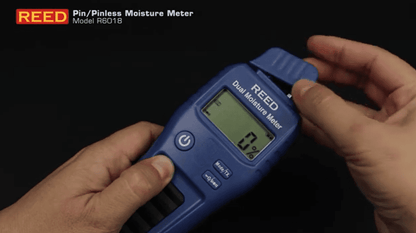 Blue REED r6018 Dual Moisture Meter being held by hands with a dark background