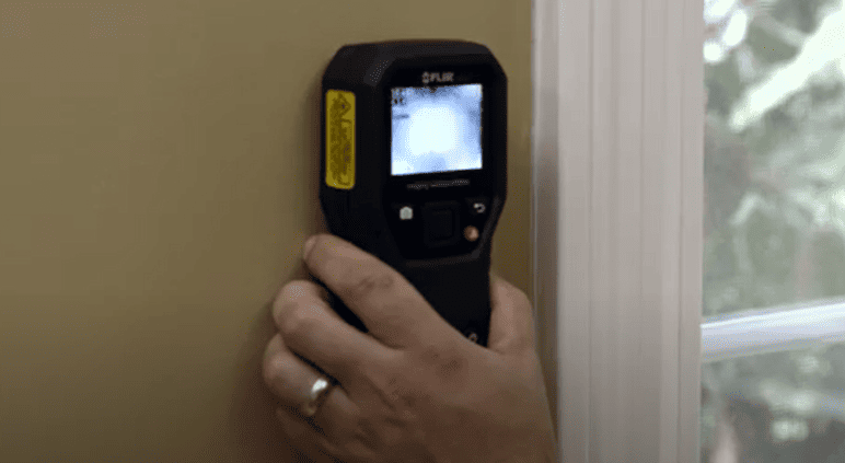 Flir MR160 hand holding a thermal imaging device against a wall