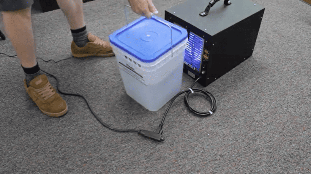 Person using a International Ozone Titan 2000 and a white Titan Maximizer with a blue lid on a gray floor.