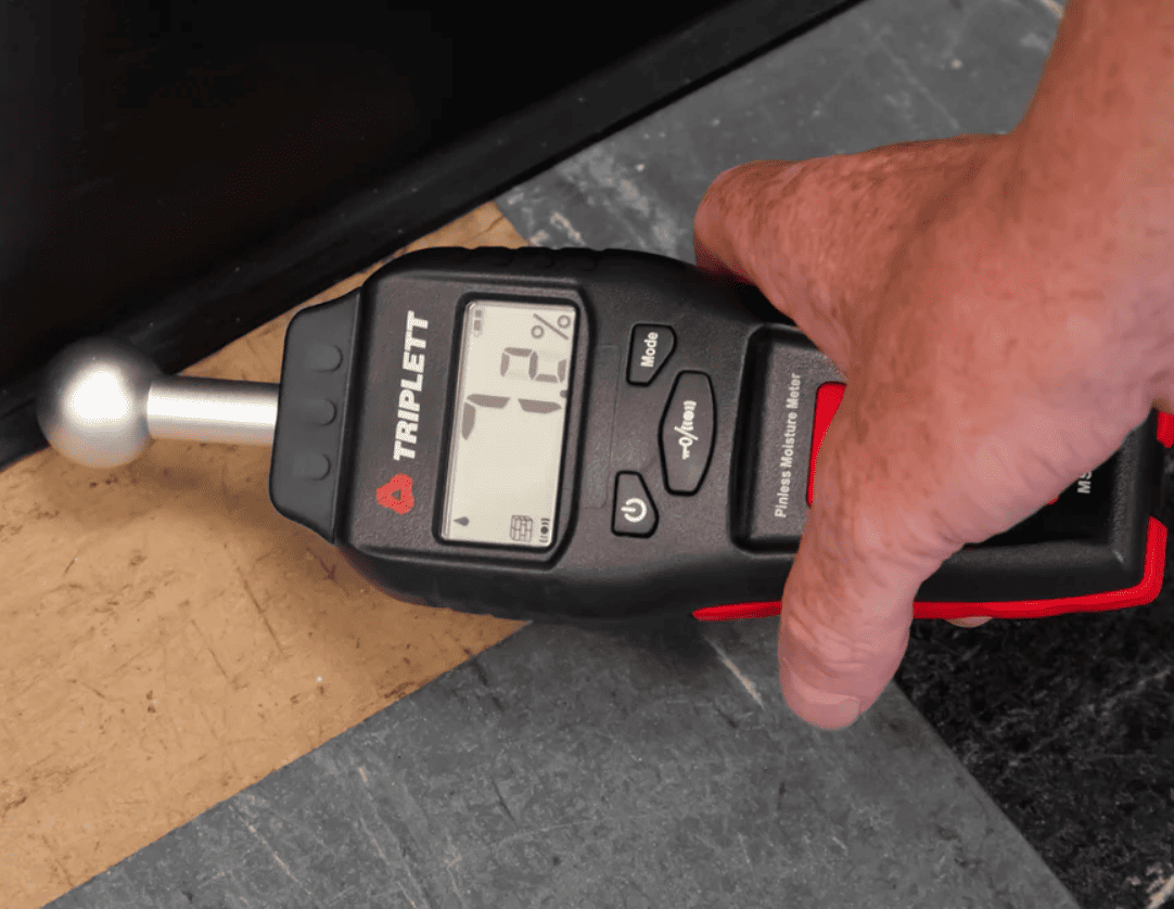 Hand holding a Triplett ms300 digital moisture meter on a concrete surface