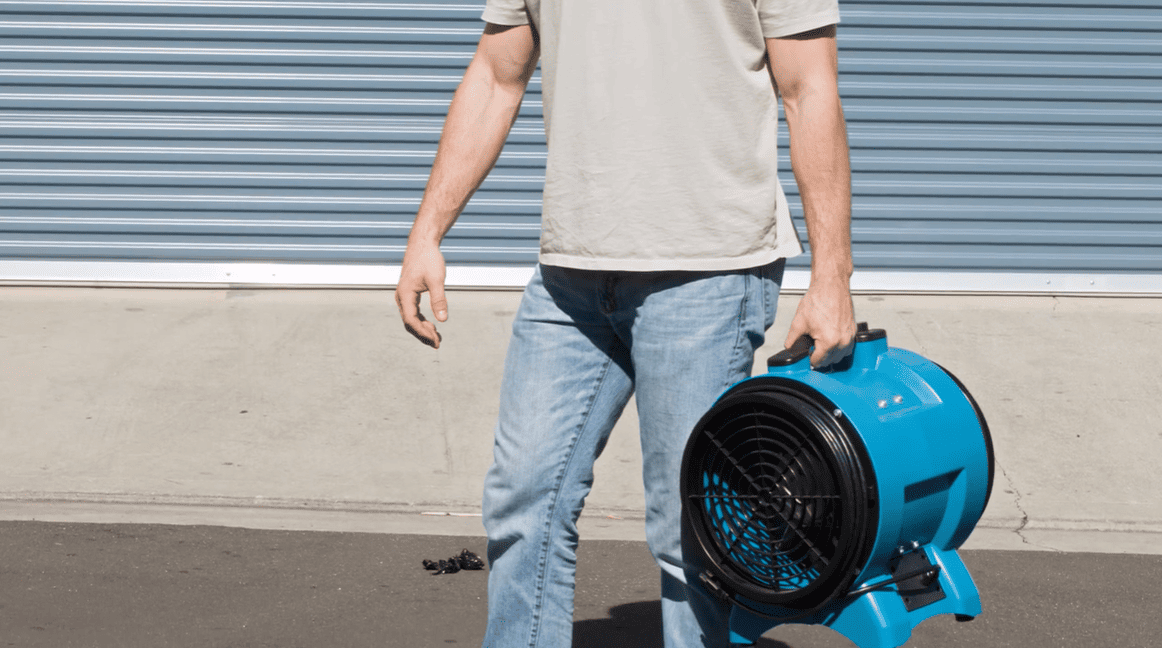 Person holding a XPOWER x8 industrial fan against a gray wall.