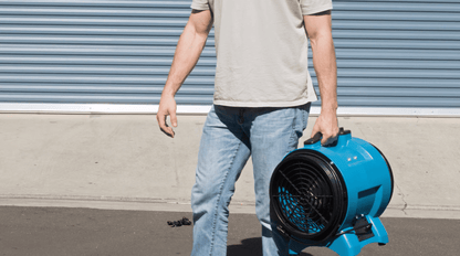 Person holding a XPOWER x8 industrial fan against a gray wall.