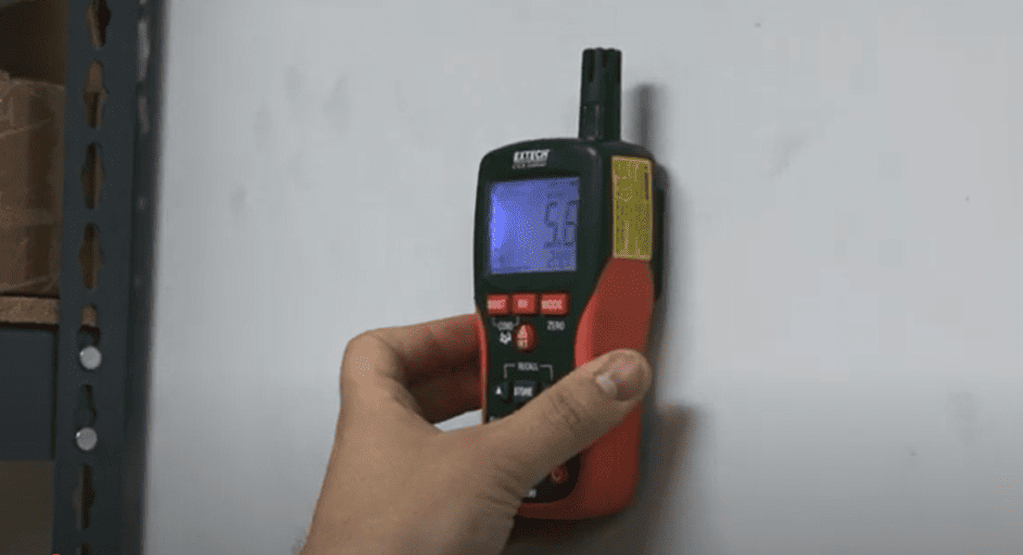 Hand holding a extech moisture meter mo290 digital device against a white wall