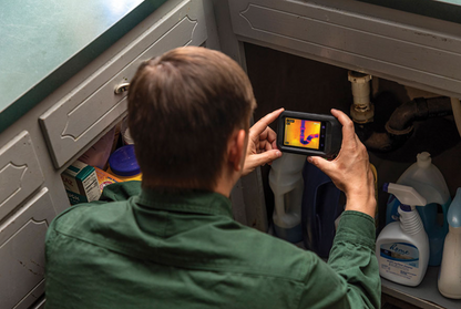 Person using a smartphone with flir c3 x thermal imaging app to inspect kitchen cabinets.