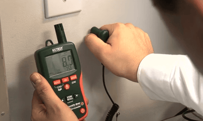 Person using a digital mo290 extech to measure moisture on a wall.
