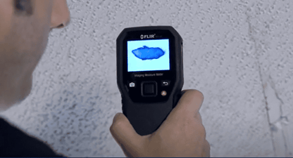MR160 person using a Flir MR160 thermal imaging device on a textured wall.