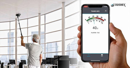 Person using a smartphone app for humidity measurement in an office setting with Tramex ME5 branding.